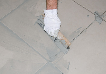 Laying floor tiles, tiler filling up joints between ceramic tiles with a rubber squeegee