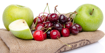 Ripe green apples and red cherries on a burlap, isolated on whiteの写真素材