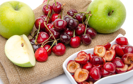 Composition with ripe green apples and cherries on a burlap and a cup of pitted cherriesの写真素材