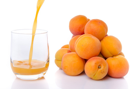 Apricot juice poured into a glass near a heap of apricots, isolated on whiteの写真素材