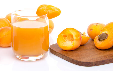 Glass of apricot juice with whole and sliced apricots, isolated on whiteの写真素材