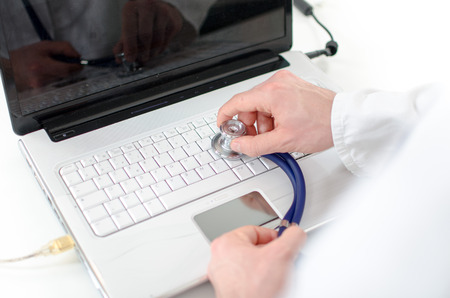 Hand holding a stethoscope on a white laptop keyboard