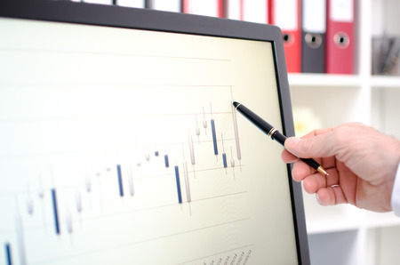 Hand showing stock exchange data graph with a pen on a screen
