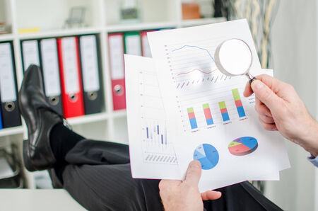 Relaxed businessman analysing a financial graph with a magnifying glassの写真素材