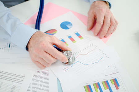 Businessman analysing a financial graph with a stethoscopeの写真素材