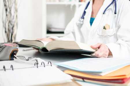 Female doctor reading a medical book at her deskの写真素材