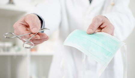 Doctor holding a surgical mask and a clamp in his officeの写真素材