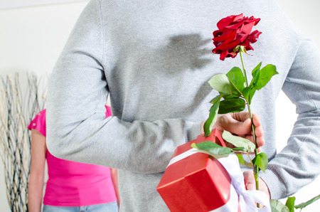 Man holding a rose and a gift behind his back for Valentine's dayの写真素材