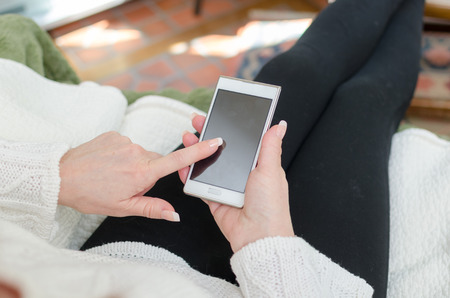 Woman sitting on a sofa using a smartphoneの写真素材