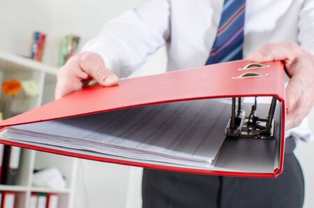 Businessman holding a red binder at officeの写真素材