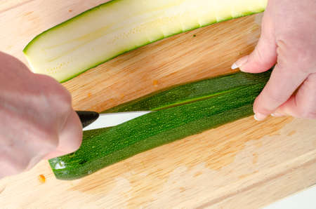 Hands of woman cutting zucchini on wooden boardの写真素材