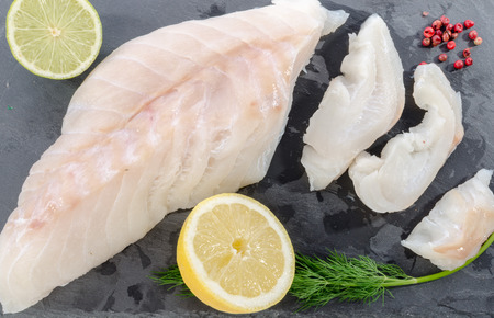 Fresh raw cod fillet on a slate plate, top view