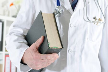 Doctor holding a medical book at officeの写真素材