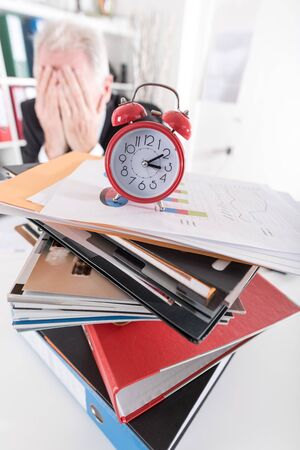 Alarm clock on stack of folders with stressed businessmanの写真素材