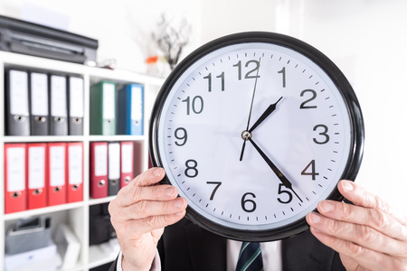 Businessman holding a clock in front of his headの写真素材