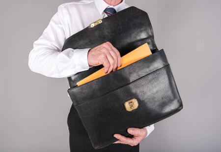 Businessman taking a folder out of his briefcase, isolated on greyの写真素材