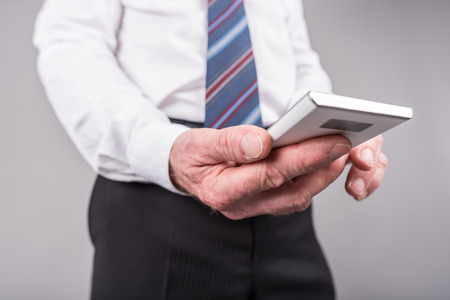 Businessman standing, using his smartphone, isolated on greyの写真素材