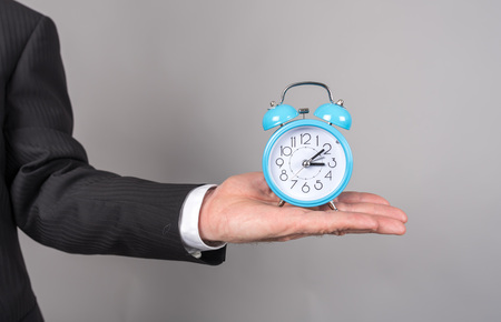 Businessman hand holding a clock, isolated on greyの写真素材