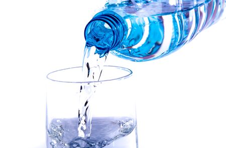 Water poured from a plastic bottle into a glass, isolated on white