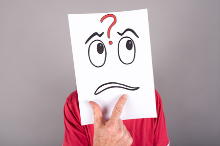 Man behind a paper with a questioning expressionの写真素材