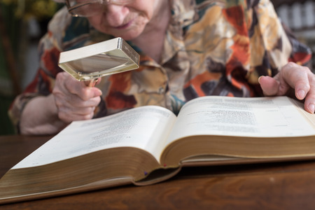 Old woman reading a book with a magnifying glassの写真素材