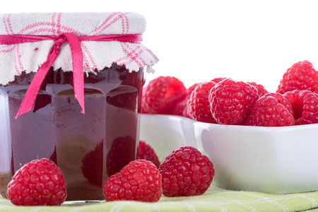 Raspberry jam jar with fresh raspberries on white background