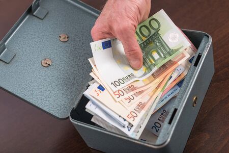 Hand withdrawing money from a metal boxの写真素材