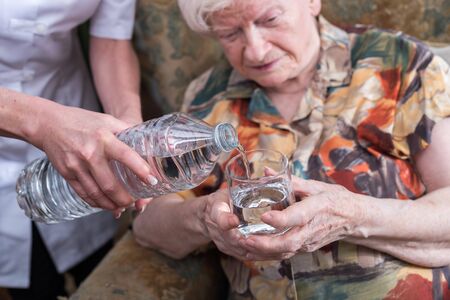 Nurse pouring water into a glass for a old womanの写真素材