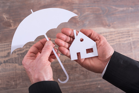 Hands holding a house and an umbrella - insurance conceptの写真素材