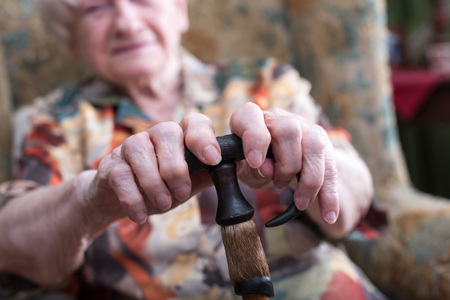 Old woman sitting with her hands on a cane
