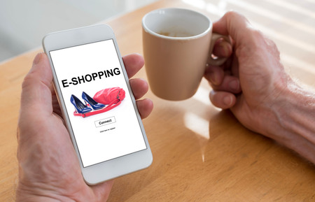 Male hands holding a smartphone with e-shopping concept and a cup of coffeeの写真素材