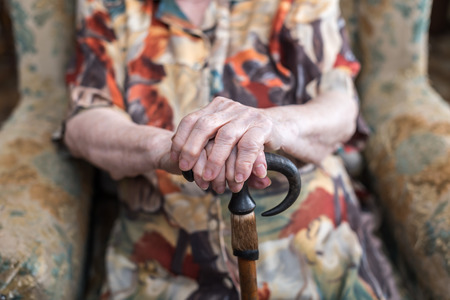 Old woman sitting with her hands on a caneの写真素材