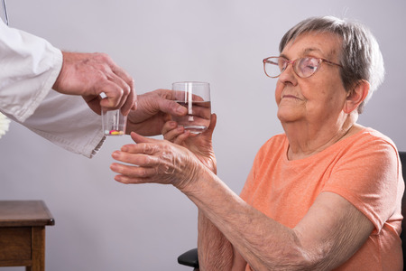 Doctor giving medicine pills to an elderly womanの写真素材