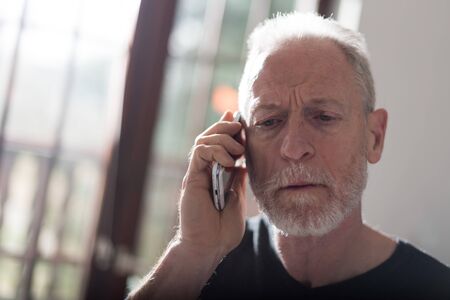 Senior man talking on phone at home, hard light effect