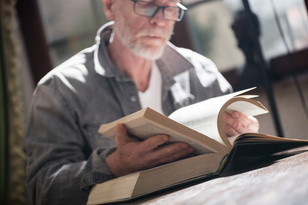 Senior man reading a book at home, hard light effectの写真素材