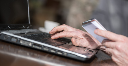 Hand typing on a laptop and holding a notepadの写真素材