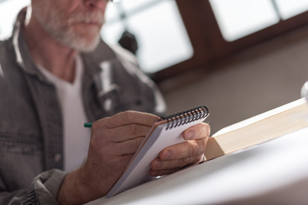 Senior man taking notes at home, hard light effectの写真素材