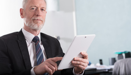 Portrait of senior businessman working on tablet at officeの写真素材