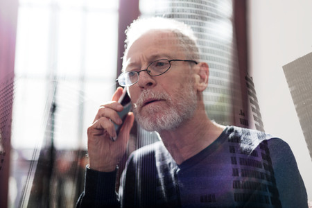 Senior businessman talking on phone at office, double exposureの写真素材