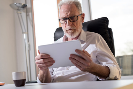 Senior businessman using a digital tablet in office, hard light