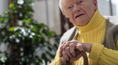 Old woman sitting with her hands on a cane