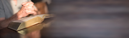Man praying with his hands over a bible on blurred backgroundの写真素材