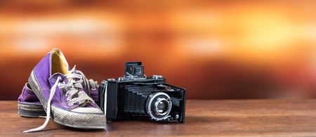 Old used purple sneakers with old camera on blurred background