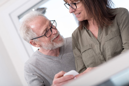 Mature couple using mobile phone at homeの写真素材