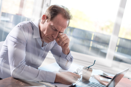Tired businessman rubbing his eyes sitting in office, light rays effect