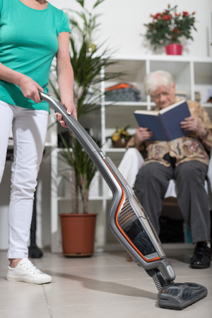 Home helper vacuuming for elderly womanの写真素材