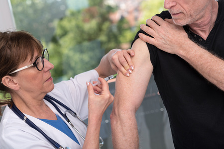 Female doctor vaccinating a senior manの写真素材