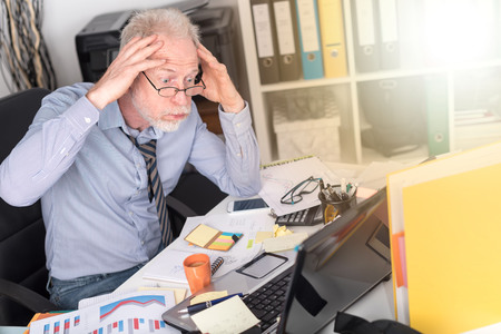 Overworked businessman sitting at a messy desk in office, light effect