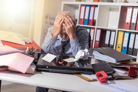 Overworked businessman sitting at a messy desk in office, light effectの写真素材