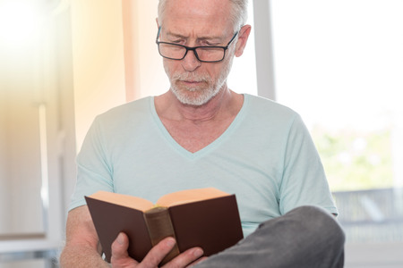 Portrait of mature man reading a book at home, light effectの写真素材